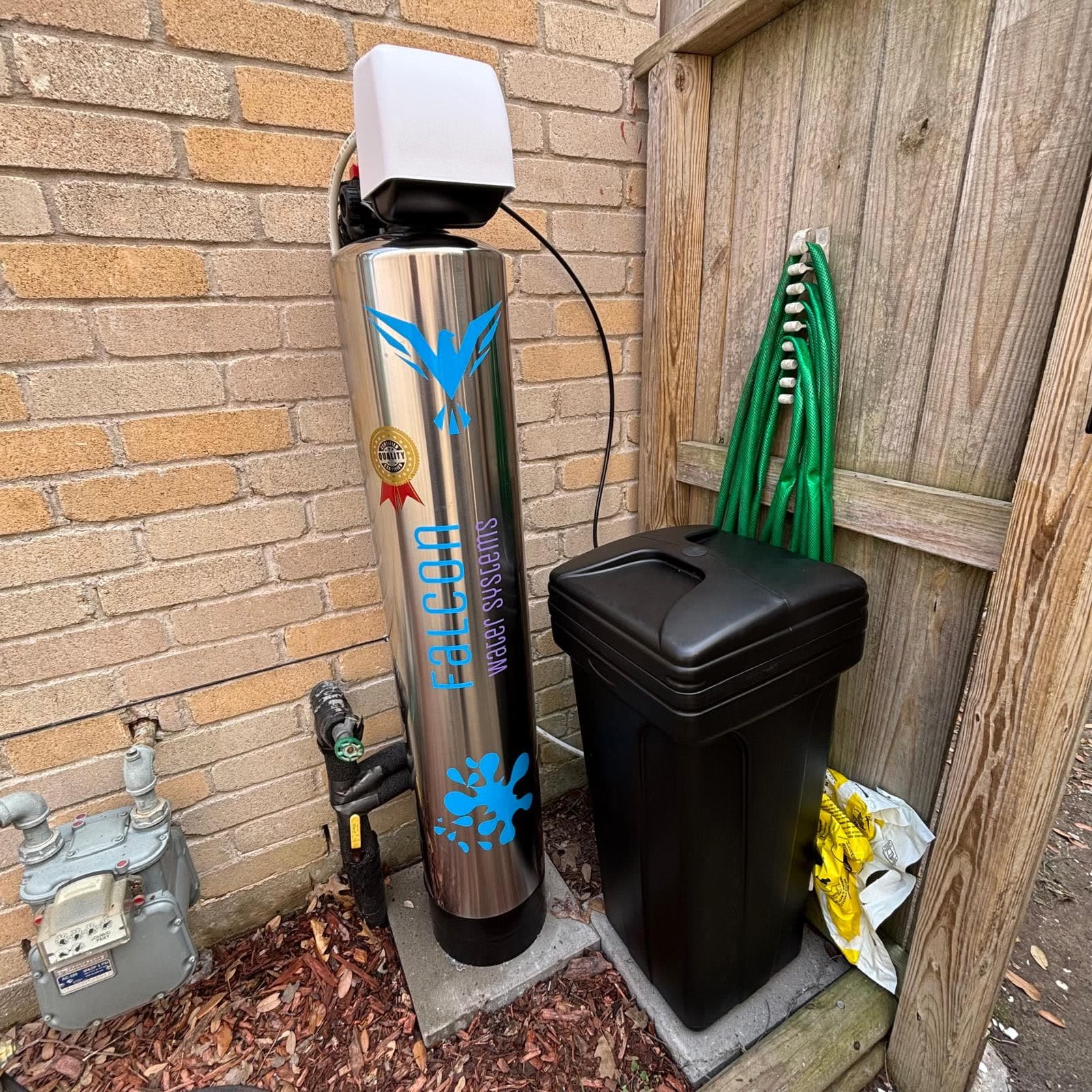 Stainless steel Falcon whole-house filtration tank with the teal falcon logo, installed outdoors