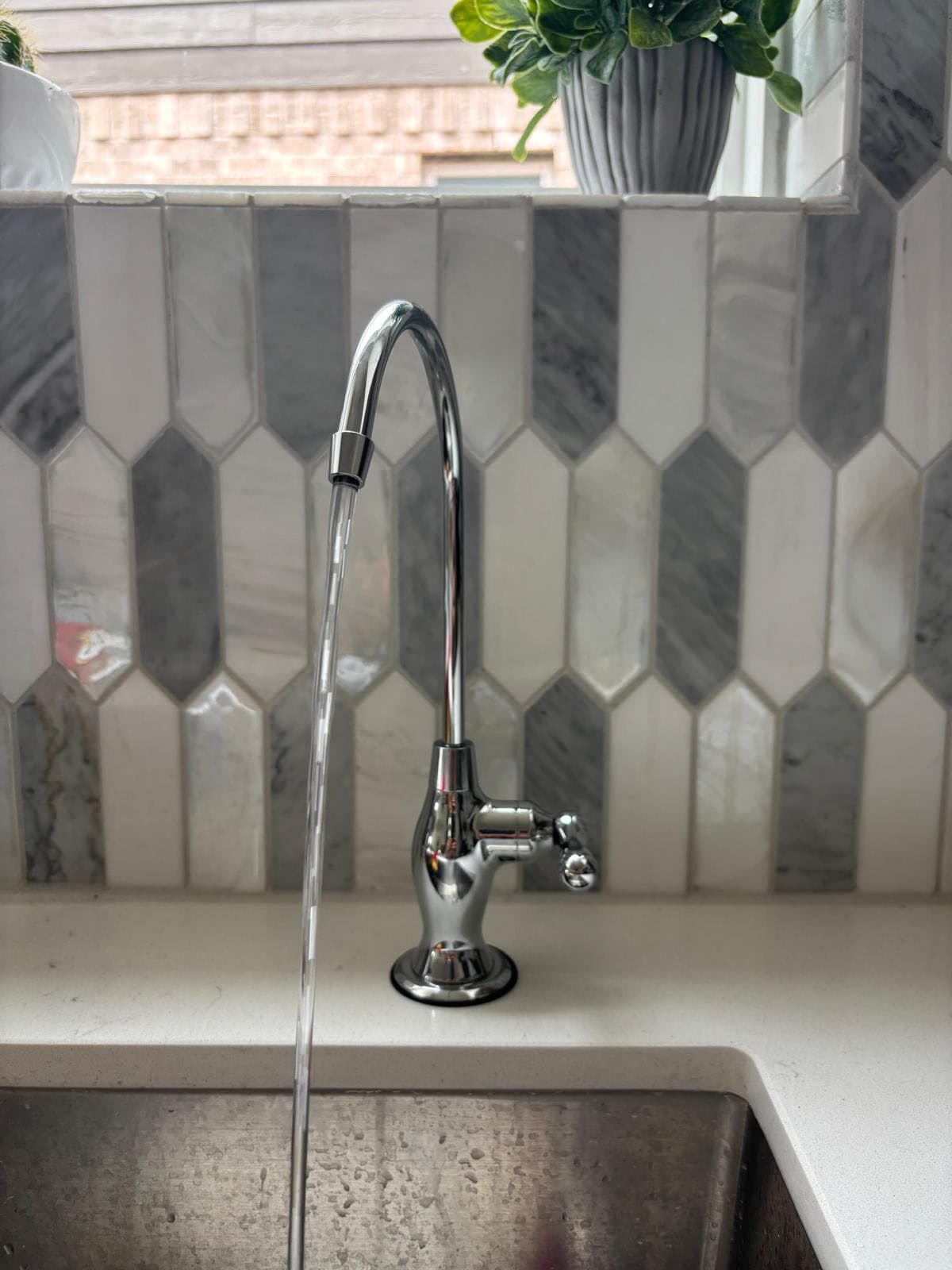 Chrome designer reverse osmosis faucet pouring filtered water against a marble backsplash